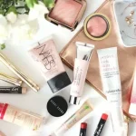 A collection of women’s beauty and skincare products arranged neatly on a white background, including lotion, lipstick, and makeup brushes